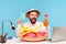 Cheerful bearded man in funny hat sitting at workplace with lifebuoy and toy airplane holding in hands passport and bottle with