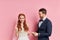 Cheerful beautiful woman and man wearing tux and white wedding dress  over pink ackground