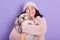 Cheerful beautiful young girl holding her dog in both hands, hugging pet much, being fond of animals, wearing pink faux fur coat