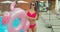 Cheerful beautiful young woman walking by the pool holding sprinkled pink inflatable flamingo float in summer. Pool