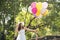 Cheerful beauty woman holding balloons relax sitting under big tree in green park with happiness. Woman Hands holding vibrant air