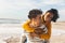 Cheerful biracial man giving piggyback ride to girlfriend at beach against sky on sunny day