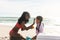 Cheerful biracial woman applying sunblock lotion on daughter\\\'s forehead at beach during sunny day