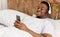 Cheerful Black Guy Using Smartphone Wearing Headphones Lying In Bed