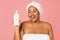 Cheerful Black Lady Holding Body Lotion Bottle Over Pink Background