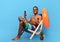 Cheerful black man in swimwear sitting in lounge chair with cellphone, recommending new mobile app, showing thumb up