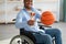 Cheerful black sportsman in wheelchair showing basketball and trophy, happy over his victory at home, selective focus