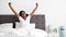 Cheerful black woman enjoying happy morning, stretching in bed