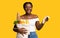 Cheerful black woman holding supermarket bill and bag with groceries, yellow background