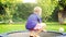 Cheerful blond boy jumping on trampoline in the summer garden