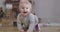 Cheerful blond Caucasian baby girl with grey eyes crawling to camera on the floor. Cute child having fun at home