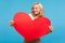 Cheerful blond lady holding in hands big red paper heart looking at camera with toothy smile, love and happiness