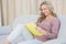 Cheerful blonde on couch reading notebook