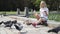 Cheerful blonde girl feeding pigeons bread in the park near the lake.