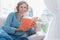 Cheerful blonde woman sitting on her couch holding a book