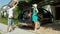 Cheerful blonde woman watches her boyfriend close the trunk of their black SUV.