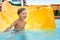 Cheerful blue-eyed kid on a water slide in the water park, a little boy merrily slides into the water along the slide in