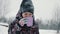 Cheerful boy drinking hot tea from cup in snowy forest at winter walk. Boy enjoying winter tea while walking at cold day