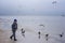 A cheerful boy feeds gulls on the seashore in winter, spring or autumn. many gulls are flying around. Cold day by the sea.