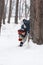 Cheerful boy peeks out from behind tree. Child in knitted hat walks through winter snow-kept park. Vertical frame