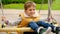 Cheerful boy sitting in wicker rope swing and riding up high. Active child, sports and development, kids playing outdoors