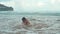 Cheerful boy spending time at seashore. Joyful teenager splashing in water.