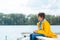 Cheerful boy wearing yellow raincoat sitting near river