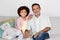 Cheerful Brazilian grandfather and grandson sitting together on couch indoors