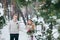 Cheerful bride and groom in beige knitted pullovers are walking in snowy forest. Selective focus on bride. Artwork