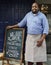 A cheerful business owner standing with open blackboard