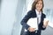 Cheerful businesswoman holding folders and drinking a coffee at work. One female businessperson carrying files and