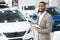 Cheerful Car Dealer Gesturing Showing Brand-New Automobile Standing Indoors