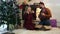 Cheerful Caucasian blond woman and bearded man sitting in front of fireplace and Christmas tree and playing ukulele