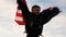 Cheerful Caucasian boy 6-7 years old runs holding an American flag. Independence day theme. Child waving American flag in the stre