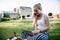 Cheerful Caucasian female freelancer sitting on summer grass