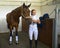 Cheerful Caucasian girl in formal wear tacking up her beautiful brown stallion.