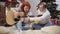 Cheerful Caucasian husband teaching positive wife playing guitar on New Year\'s eve. Happy carefree spouses celebrating