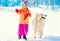 Cheerful child with white Samoyed dog on leash at snow winter day