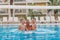 Cheerful children with their father jump in the outdoor blue pool on vacation