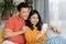 Cheerful chinese lovers using smartphone, home interior