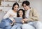 Cheerful chinese millennial mom, dad and teen daughter look at tablet, surfing, shopping online together