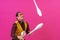 Cheerful circus performer skillfully juggling a number of clubs isolated on pink background