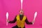 Cheerful circus performer skillfully juggling a number of clubs isolated on pink background