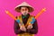 Cheerful circus performer with a sombrero holding toy water guns on pink background