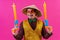 Cheerful circus performer with a sombrero holding toy water guns on pink background