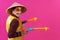 Cheerful circus performer with a sombrero holding toy water guns on pink background