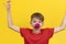 Cheerful clown child. Bright Red t-shirt and nose. Portrait on yellow background