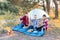 A cheerful company of two girls and a boy on a picnic in the middle of the forest. Children hold sausages on skewers to roast on