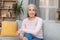Cheerful confident calm pretty european senior female with gray hair sits on sofa, enjoys free time