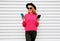 Cheerful cool girl holding two smartphone and looking at them in city on white wall